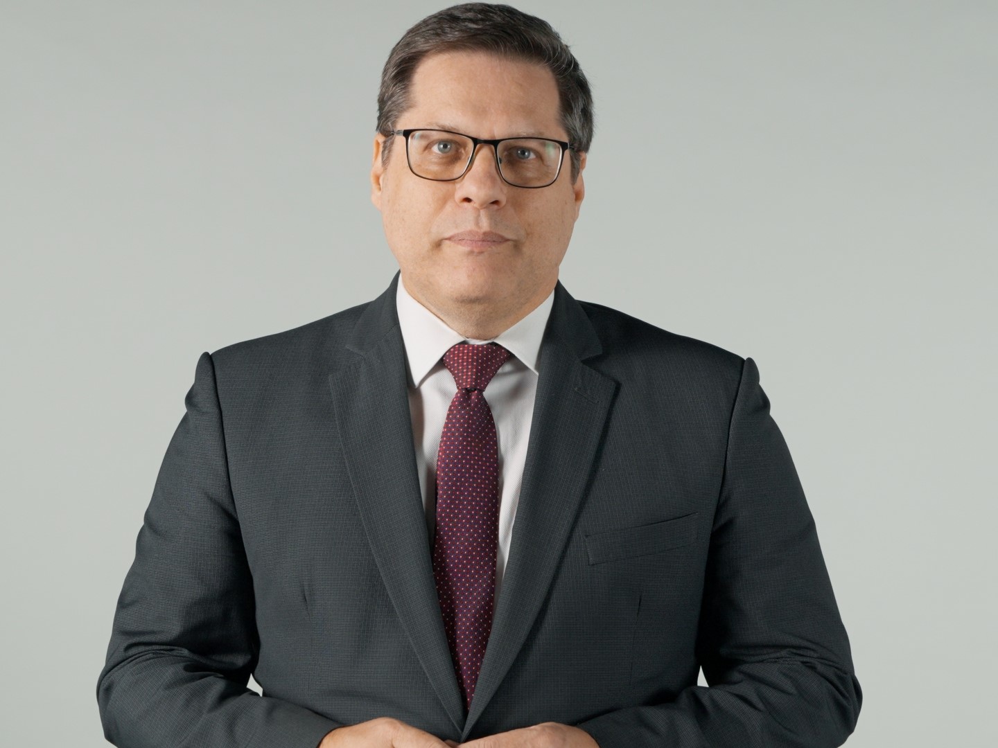Um homem de terno e gravata em pé com as mãos cruzadas.