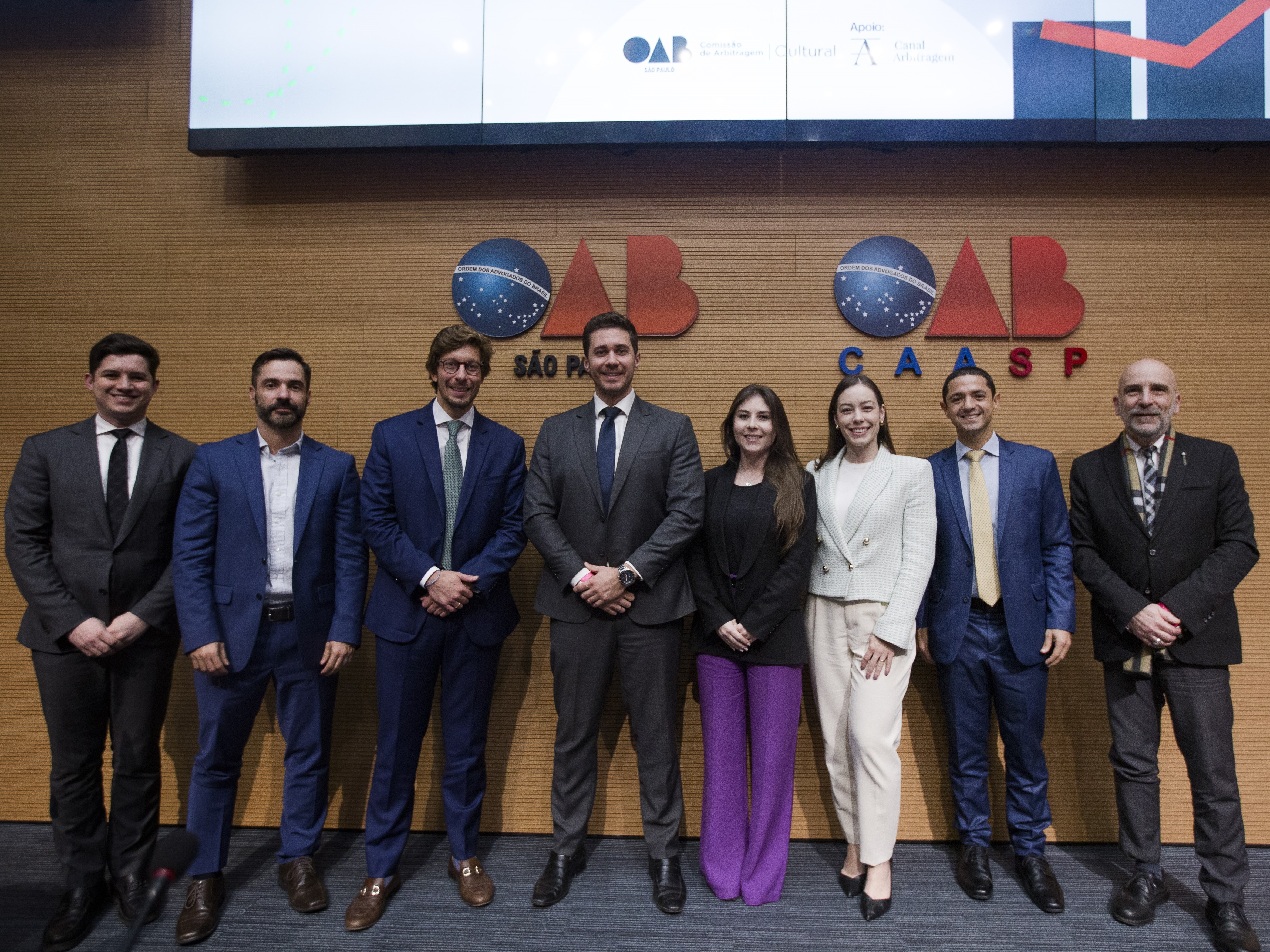 Gurpo de oito pessoas, seis homens e duas mulheres, em pé, a frente de um painel de madeira com os escritos OAB São Paulo e OAB CAASP.