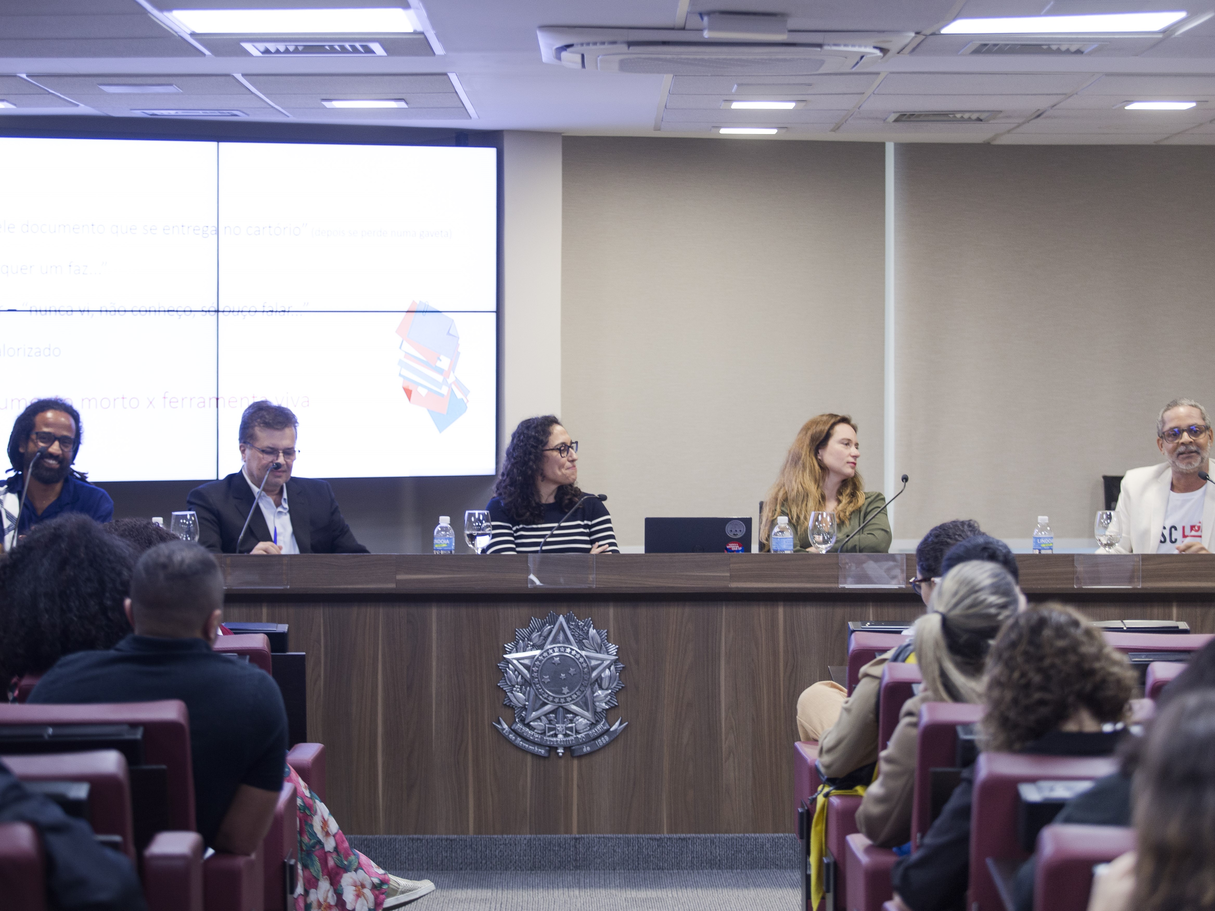 Um grupo de pessoas sentadas em uma mesa em frente a uma tela.
