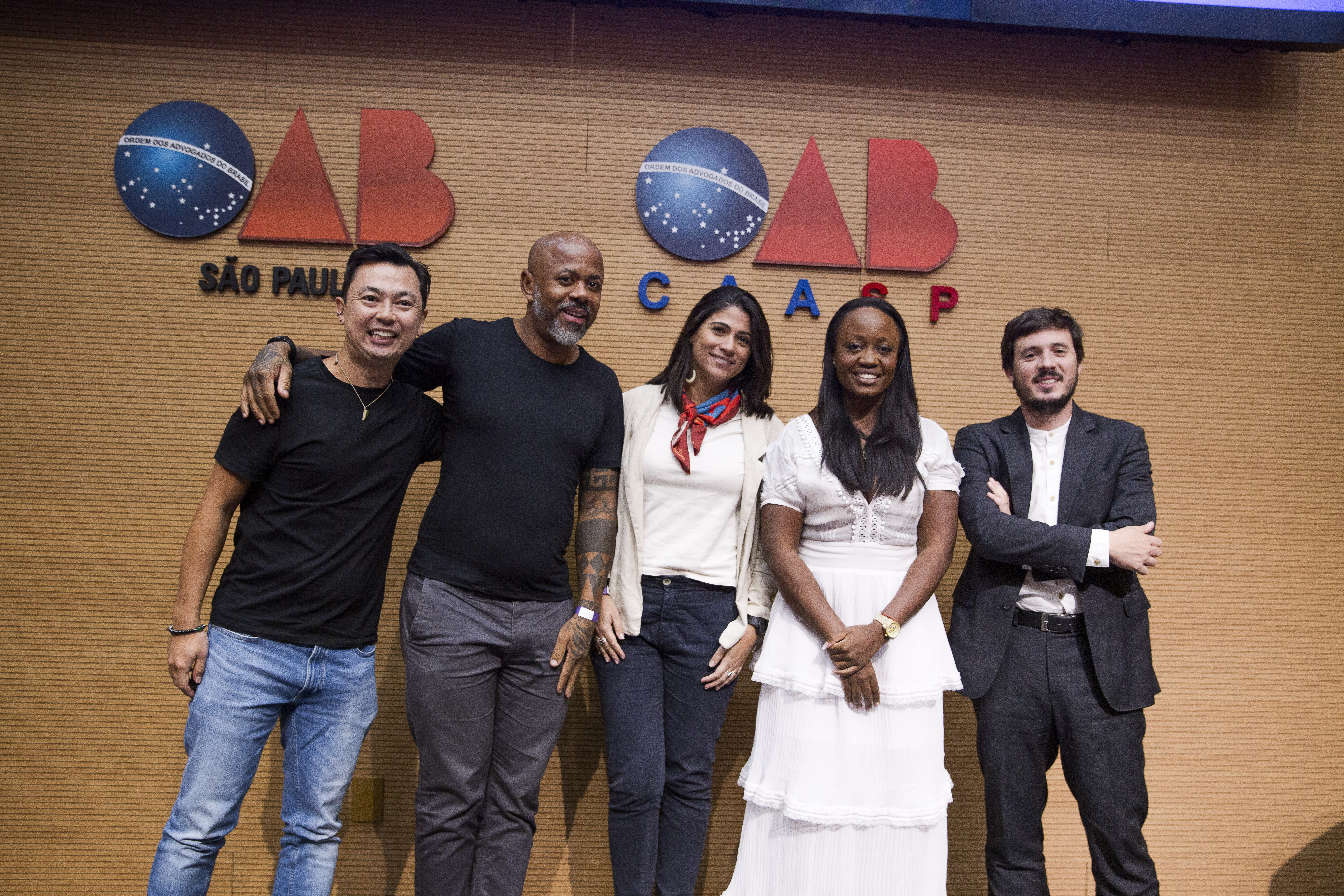 Cinco pessoas em frente a uma parede com os símbolos escritos OAB São Paulo e OAB CAASP, sorrindo e posando para foto.