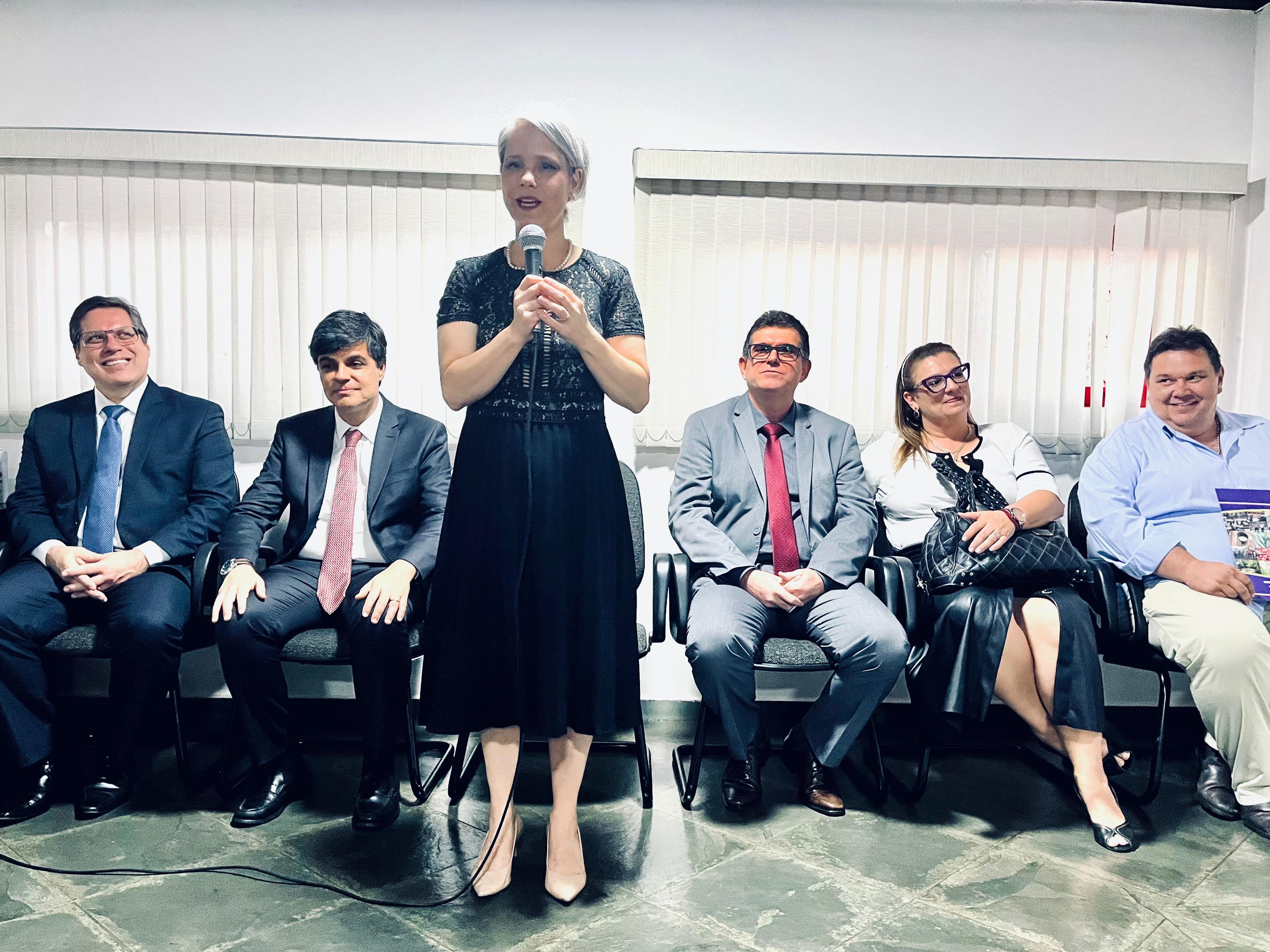 Uma mulher de vestido preto em pé na frente de um grupo de pessoas.